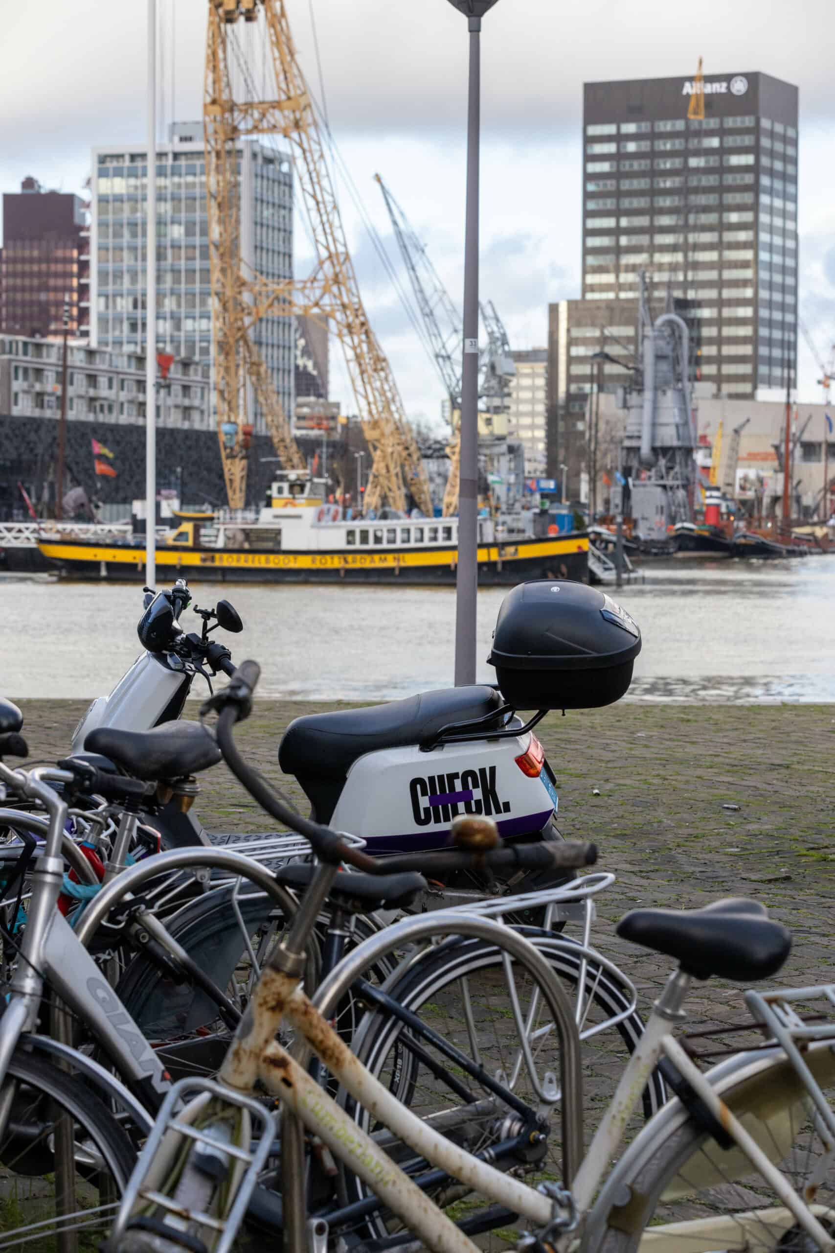 Fietsen en deelscooter geparkeerd bij de rivier met uitzicht op de skyline en schepen in Rotterdam.